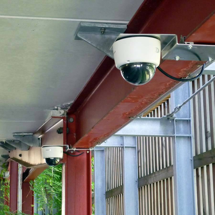 Dome-Kameras zur Videoüberwachung an eines Parkhauses Zwei Dome-Kameras zur Videoüberwachung eines Parkhauses sind unter einer Decke an Stahlträgern montiert, mit sichtbaren Kabelverbindungen.