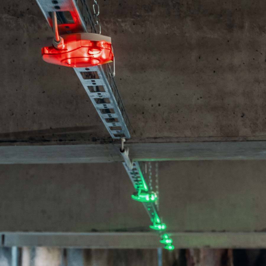 ETEC Verkehrstechnik: Sensorbasiertes LED-Parkleitsystem in einem Parkhaus Rote und grüne LED-Leuchten an einer Metallschiene unter der Decke eines Parkhauses zeigen belegte und freie Stellplätze an.