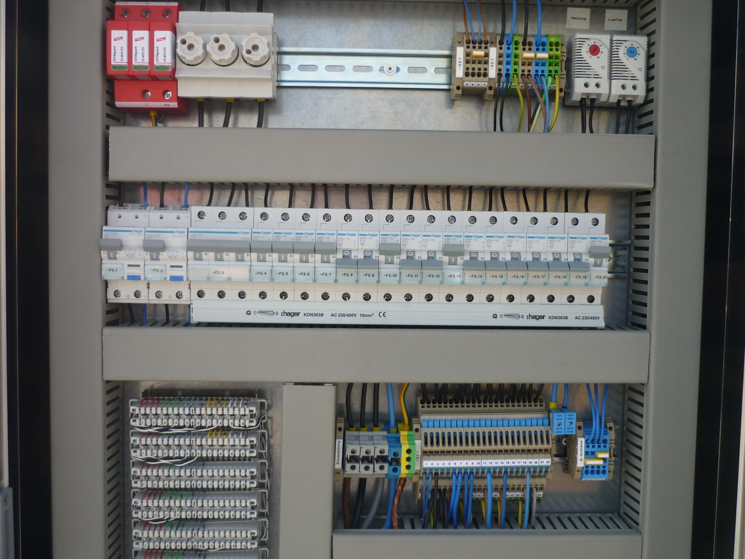 Übersichtlich verdrahteter Elektroverteilerschrank Geöffneter Verteilerschrank mit mehreren Sicherungsautomaten, Reihenklemmen, Überspannungsschutz und Thermostaten, ordentlich verdrahtet.